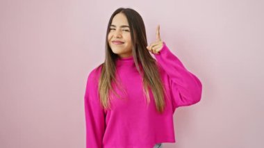 Pembe izole bir arka plan üzerinde duran neşeli, genç Latin bir kadın, kendine güvenerek bir parmağını kaldırıp süveter giyiyor. Güzel bir başarı fikri onu ışıldatıyor.!