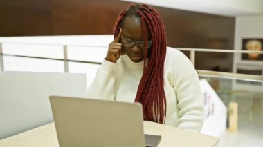 Ofis masasında gözlük takan ve süveter giyen düşünceli bir Afrikalı kadın..