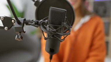 Gülümseyen genç İspanyol kadın profesyonel mikrofon ve kulaklıkla modern bir kapalı mekan müzik stüdyosunda kayıt yapıyor..