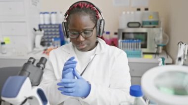 Bir laboratuvar ortamında mikroskop kullanarak araştırma ve sağlık hizmetlerini anımsatan örgü ören odaklı Afrikalı kadın bilim adamı..