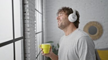 Sakallı ve kulaklıklı rahat bir adam modern, parlak bir iç mekanda kahvesini yudumluyor..