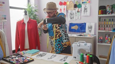 Sakallı şık bir adam renkli bir terzi stüdyosunda çizimlerinin fotoğrafını çekiyor..