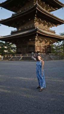 Güzel İspanyol kadın ayakta, güvenle gülümsüyor Japonya 'nın To-ji tapınağının önünde, mutluluk ve kaygısız neşe saçıyor, dostça ifadesi bu Kyoto parkını daha da eğlenceli hale getiriyor..