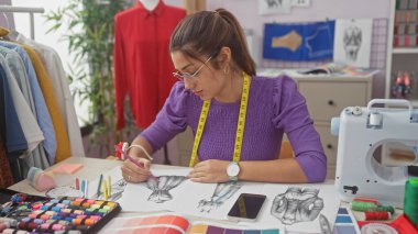 İspanyol kadın moda tasarımcısı canlı atölyesinde tekstil dolu bir elbise çiziyor..