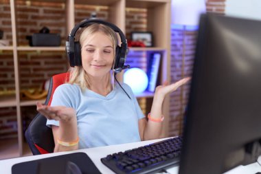 Video oyunları oynayan, kulaklık takan, avuçlarını açıp gülümseyen, sunan, reklam veren ve dengede duran beyaz bir kadın. 