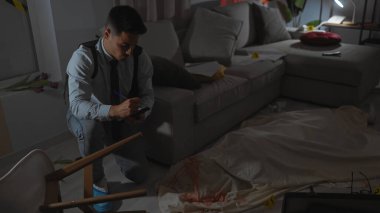 Kapalı bir suç mahallinde elinde kanlı bir çarşaf ve kanıtlarla akıllı telefon kullanan konsantre bir genç adam..