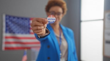 Mavi ceketli Afro-Amerikalı kadın kapalı alanda bizlere oy verdiğimi gösteriyor.