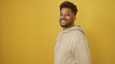 Yakışıklı siyahi adam, saf sarı arka planda güvenle gülümsüyor, pozitifliği ve gençliği çağrıştırıyor..