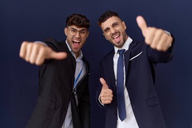 İki İspanyol iş adamı iş kıyafetleri giyip olumlu jestler yapıyorlar. Elleriyle gülümsüyorlar ve başarı için mutlular. kazanan jest. 