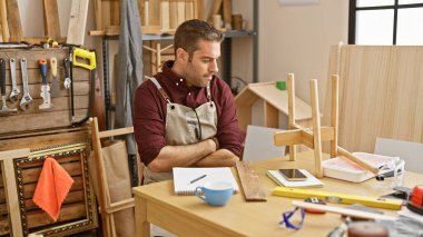 İyi donanımlı bir marangozhanede ahşap bir model tasarlayan apronlu yakışıklı bir İspanyol..