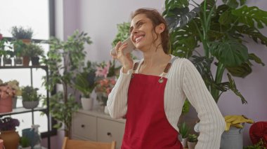 Kırmızı önlüklü, güler yüzlü bir kadın çiçekçide sesli mesajdan hoşlanır..