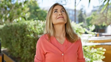 Olgun sarışın kadın yeşil bir parkta sükunetin tadını çıkarıyor.