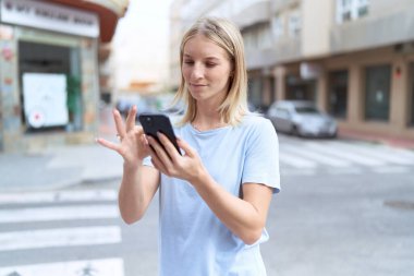 Sokakta akıllı telefon kullanan, kendine güvenen genç sarışın kadın.