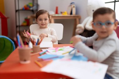 Adorable girl and boy sitting on table cutting paper at kindergarten 
