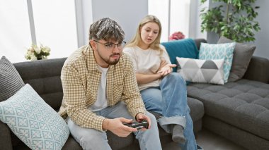 Bir kadın, modern bir oturma odasında video oyunları oynamaya odaklanmış bir adamla tartışıyor.