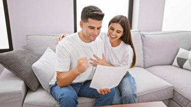 Neşeli bir çift, evdeki sevgi ve ortaklığı somutlaştıran modern bir oturma odasındaki bir kanepede bir belgeyi birlikte gözden geçirir..