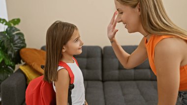 Anne ve kızı, modern bir oturma odasında neşeli bir anın tadını çıkarıyorlar. Aile sevgisini ve neşesini ifade ediyorlar..