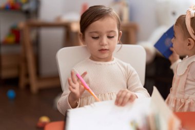 Anaokulunda masada oturmuş kağıt kesen iki küçük kız.