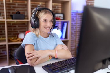 Video oyunları oynayan, kulaklık takan, kollarını kavuşturup kameraya gülümseyen beyaz bir kadın. pozitif kişi. 