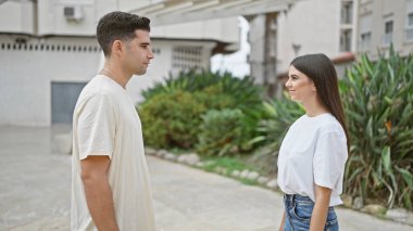 Yeşillik ve birliktelik hissini yansıtan, açık havada parkta dikilen sıradan giysili bir çift..