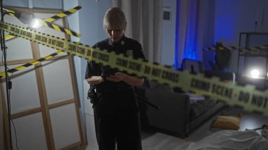 Kadın bir polis memuru, loş bir evde kapalı bir suç mahallinde kanıtları inceliyor..