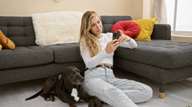 Beyaz kadın oturma odasının iç kısmında siyah köpekli akıllı telefon kullanıyor..