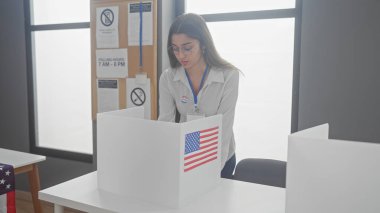 Genç bir İspanyol kadın, bayraklarla süslenmiş bir Amerikan oy kullanma merkezinde oy pusulasına bakıyor..