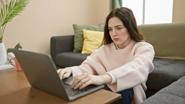 Rahat, modern bir oturma odasında dizüstü bilgisayar kullanan odaklanmış genç bir kadın..