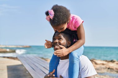 Father and daughter smiling confident holding girl on shoulders at seaside