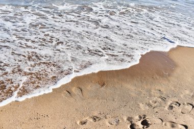 Sakin sahil sahnesi, yumuşak dalgalar ve kumlu sahil arasında belirgin ayak izleri olan arayüzü yakalıyor..