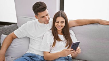 Kanepede uzanan bir çift, akıllı telefona gülümseyen bir adam, sıcak bir oturma odasında aşkı resmeden bir adam..