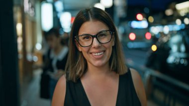 Yüksek sesle kahkahalar atan, gözlüklü, kendine güvenen İspanyol bir kadın Kyoto 'da bir sokakta neşeli bir şekilde duruyor, ışık dolu Japon şehri, pozitif olarak ışıl ışıl ve kaygısız görünüyor.