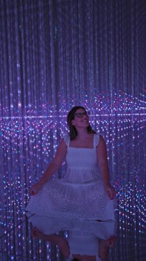 Gülümseyen güzel İspanyol kadın modern müzede fütürist sergiler sergiliyor. Lazerler, ışıklar, en iyi yenilikler.!