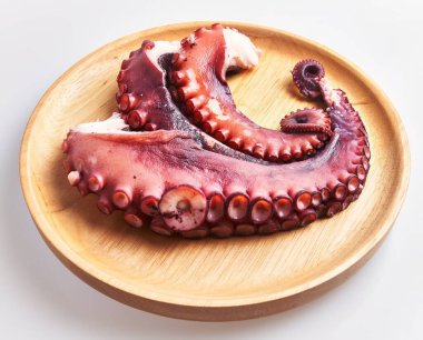 Ahşap bir tabakta sunulan çiğ bir ahtapot, deniz ürünlerinin tazeliğini beyaz bir zemine vurguluyor..