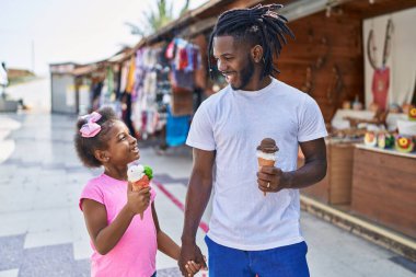 Father and daughter eating ice cream walking together at street market
