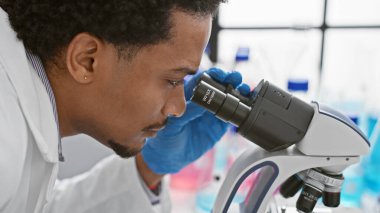 Modern bir laboratuvar ortamında mikroskopla çalışan Afrikalı bir adam..