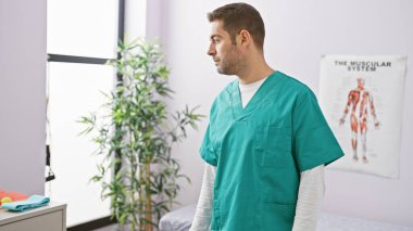 Önlüklü genç bir İspanyol adam klinikte düşünceli bir şekilde duruyor..