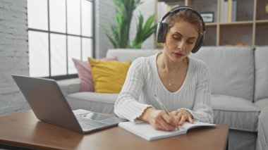 Genç bir kadın dizüstü bilgisayarla çalışırken deftere bir şeyler yazıyor..