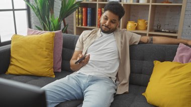 Rahat bir adam rahat bir oturma odasında renkli yastıklarla uzaktan kumandayla evde boş vaktini sergiliyor..