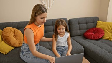 Oturma odasındaki kanepede dizüstü bilgisayar kullanan bir anne ve kız..
