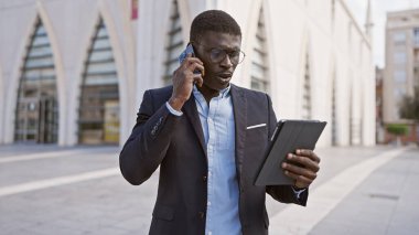 Afrika kökenli Amerikalı iş adamı, güneşli bir caddede elinde bir tablet tutarken bir telefon görüşmesi yaptı..