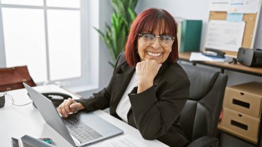 Modern ofis içinde dizüstü bilgisayarda çalışan gülümseyen olgun İspanyol kadın..