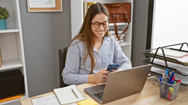 Modern ofiste bilgisayarlı akıllı telefon kullanan gülümseyen kadın.