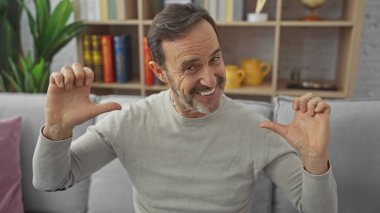 Gülümseyen orta yaşlı bir adam, küçük beden ve kapalı alanda el kol hareketi yapıyor.