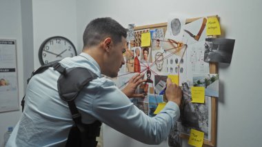 Young hispanic man analyzing crime evidence on a board at the police department. clipart