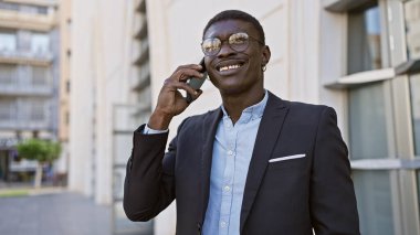Yakışıklı Afrikalı takım elbiseli adam Sunny City caddesinde akıllı telefon kullanıyor.