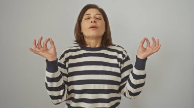 Orta yaşlı İspanyol bir kadın çizgili bir kazakla beyaz bir duvara doğru meditasyon yapıyor.
