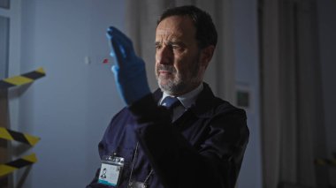 Orta yaşlı bir adam, kapalı bir mekanda suç mahallinde kanıtları analiz ediyor..