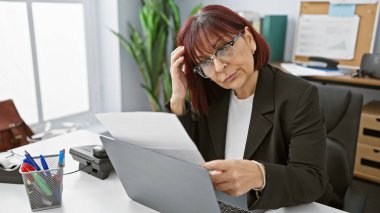 Endişeli, orta yaşlı bir İspanyol kadın ofisinde belgelere bakıyor. İşle ilgili ciddi bir sorun olduğunu söylüyor..