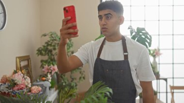 Genç adam, arka planda yemyeşil bitkiler olan canlı bir çiçekçide selfie çekiyor.